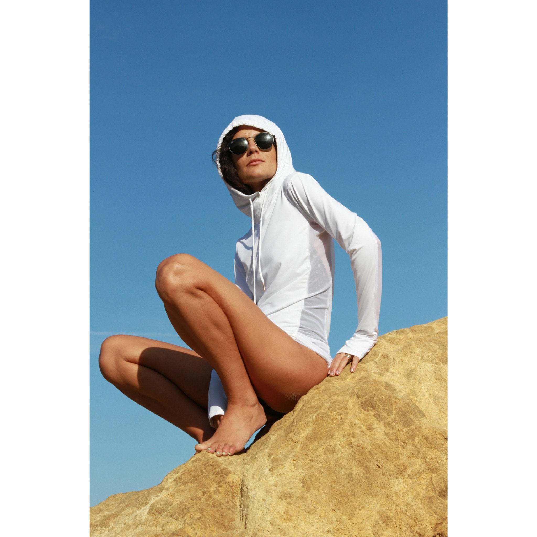 Woman on a beach wearing a long-sleeved sun protective shirt with full hood and hand protection in white.